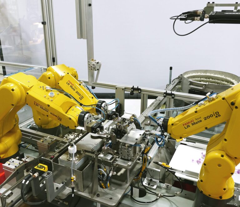 High-tech automated manufacturing setup featuring multiple yellow FANUC robotic arms assembling components on a production line with precision machinery.