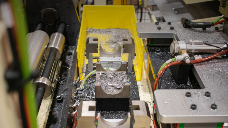 Image shows a yellow tray filled with metal shavings, surrounded by metal clamps, machinery parts and equipment. Various cables and hoses are visible.