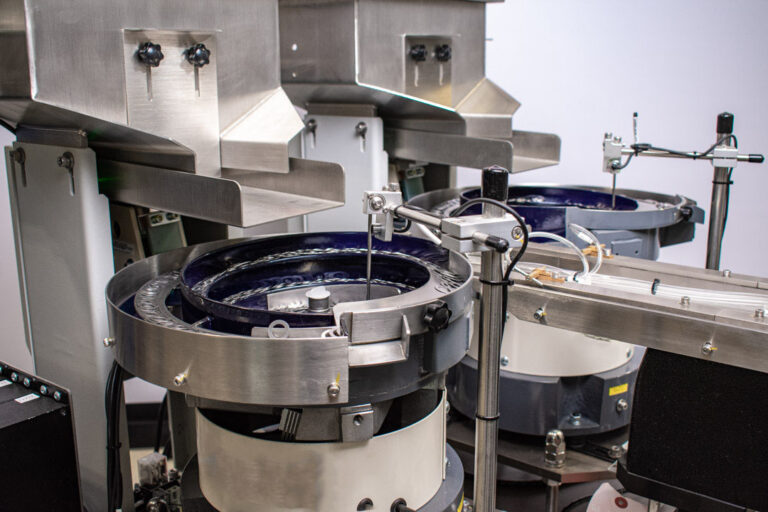 Close-up of a complex industrial machine system which includes vibratory bowl feeders that circulate parts along a track, and precision tooling for selection and placement.