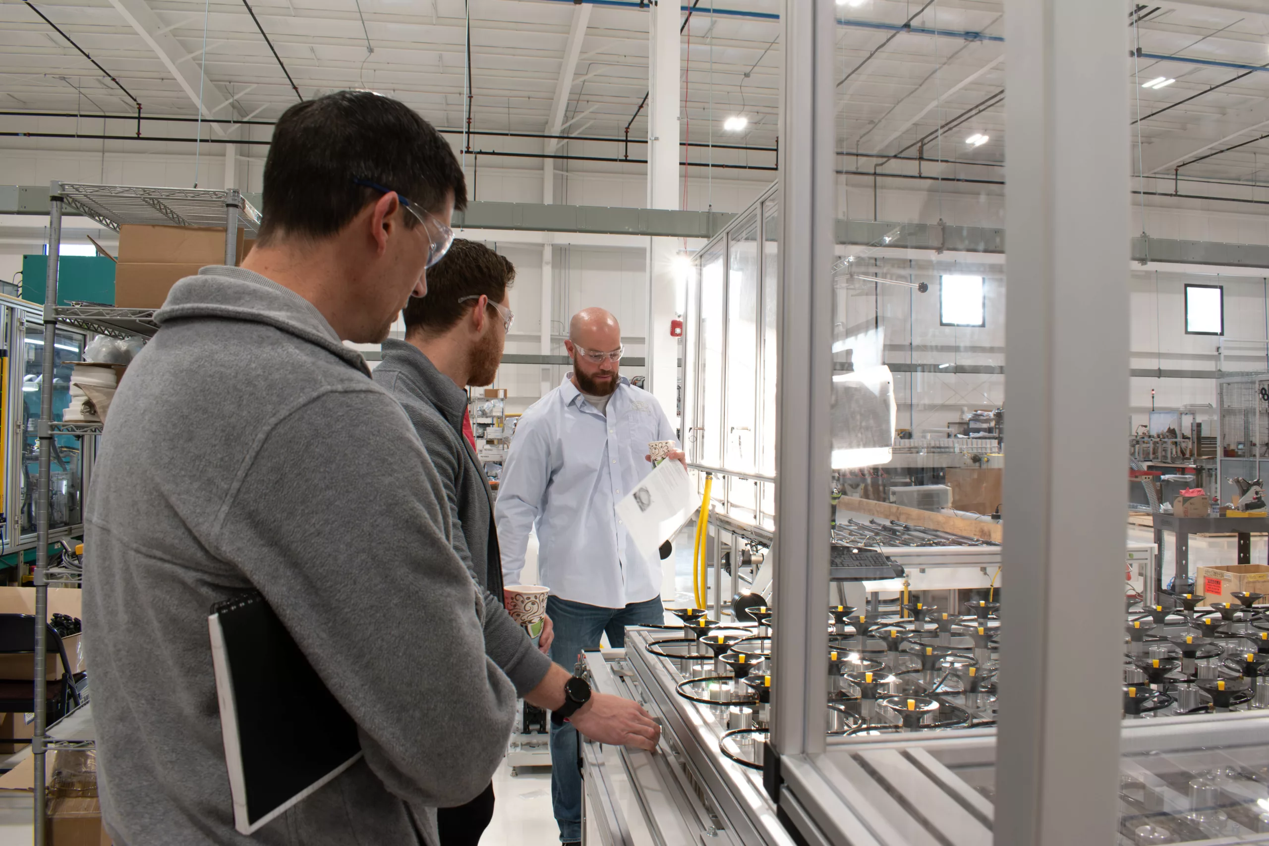 Three men on a management team standing next to a machine.