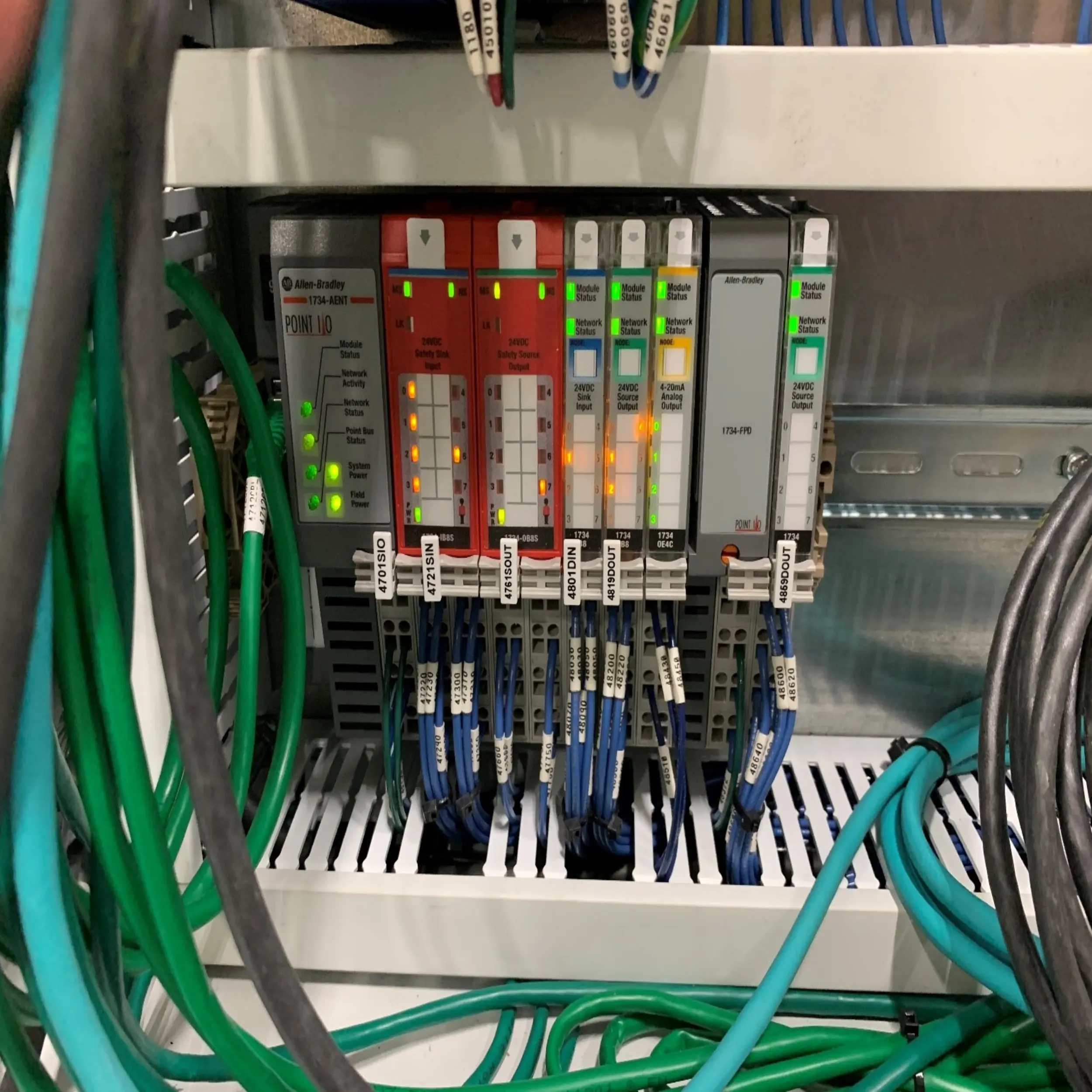 Allen-Bradley PLC (Programmable Logic Controller) system. Multiple I/O modules are visible, with numerous blue and green network cables connected. Each module has indicator lights showing its status