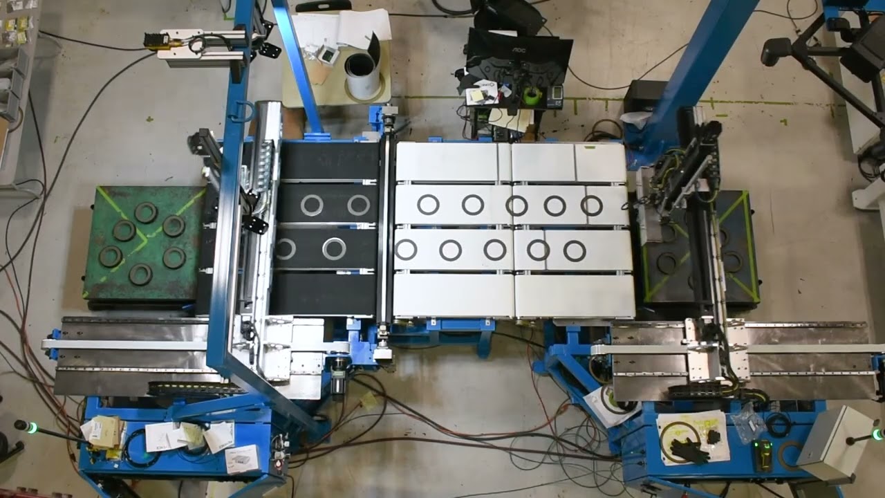 Overhead shot of a robotic industrial machine with blue metal framework, showcasing parts with circular cutouts on a conveyor belt.