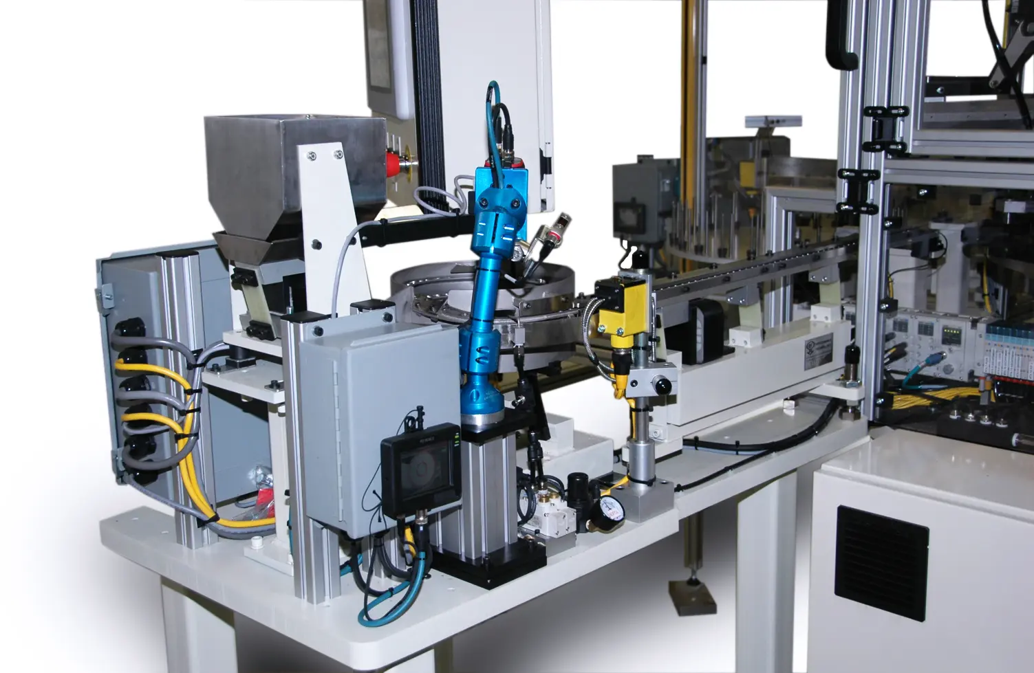 A complex automated assembly machine with a robotic arm, feeder system and electronic components. The machine includes a metal hopper, a blue industrial robotic arm, various sensors, and a conveyor belt.