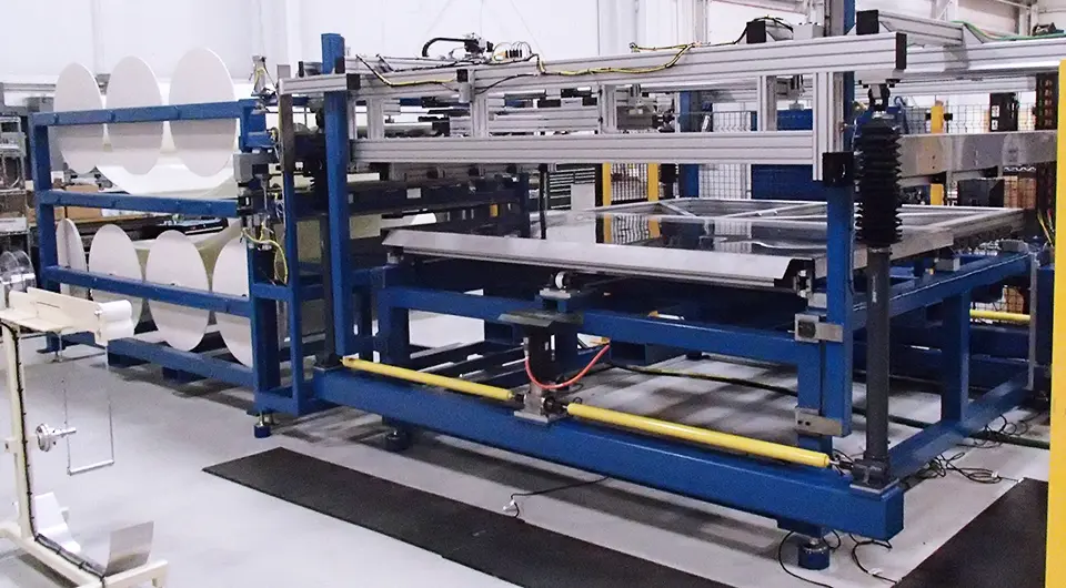 An industrial resin distribution system fills most of the frame. The system is built with blue and silver colored scaffolding. A rack to the left holds large rolls of material.