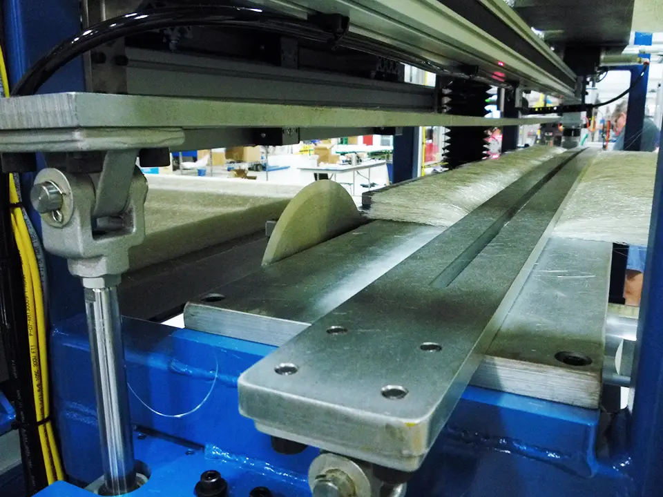 Close-up of a resin distribution system, showing multiple layers of material stacked upon a metal machinery table with blue framework. A small wedge is present.