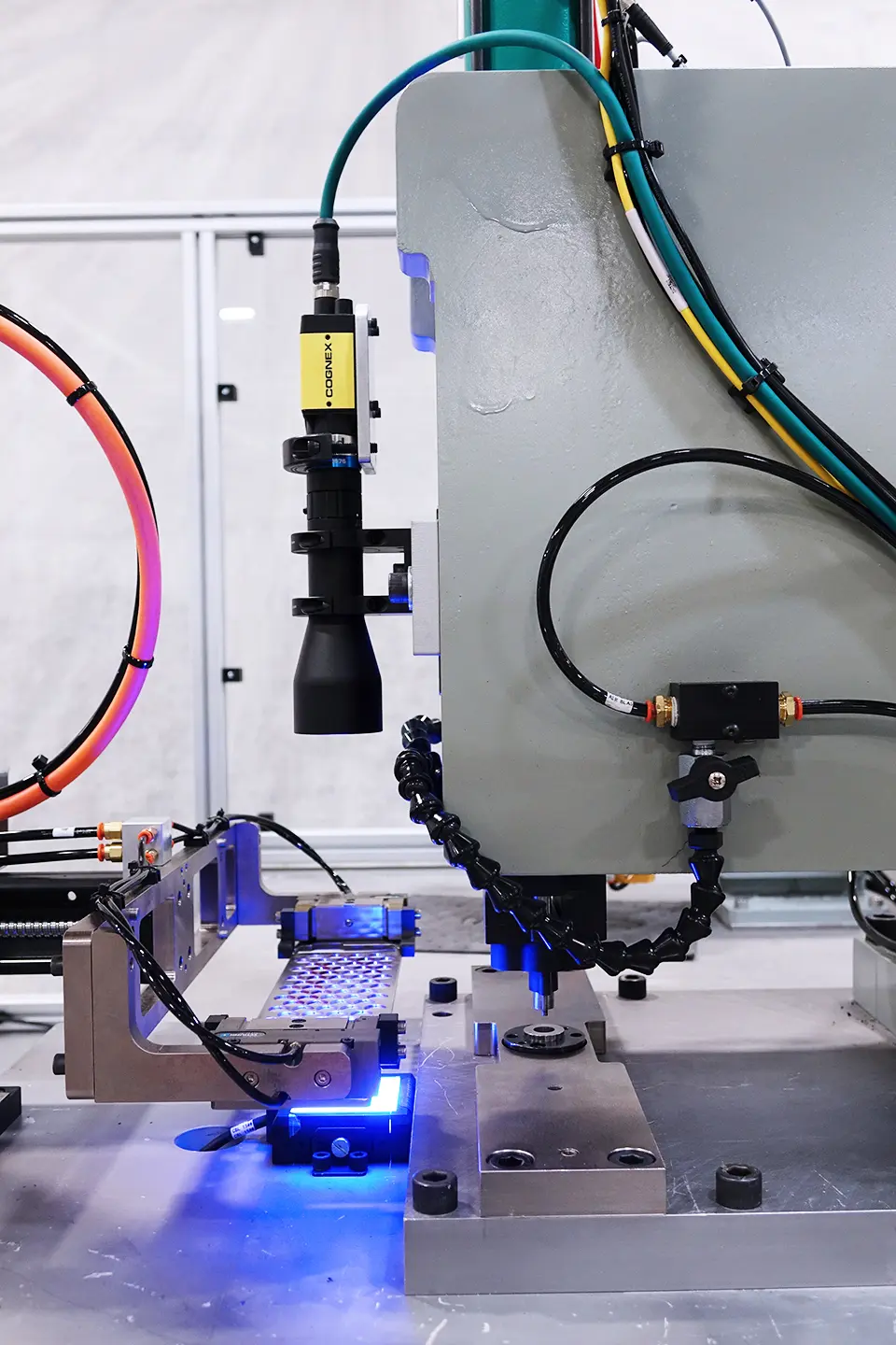 Black and yellow vertical Cognex Machine Vision Camera overhead a blue light with multi-colored wires with focus a part on a flat surface