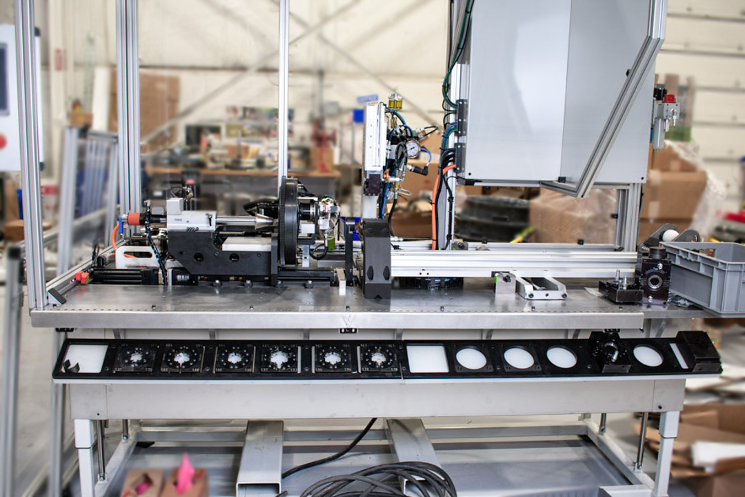 A detailed view of an automated assembly machine in a factory setting. The machine features a metal frame, various gauges and control panels, a robotic arm, and components.