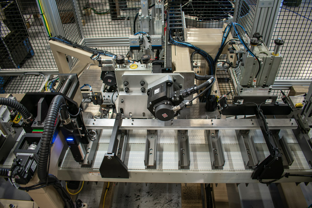 Automated assembly line with robotic arms and conveyor belt for manufacturing, enclosed by safety fencing.