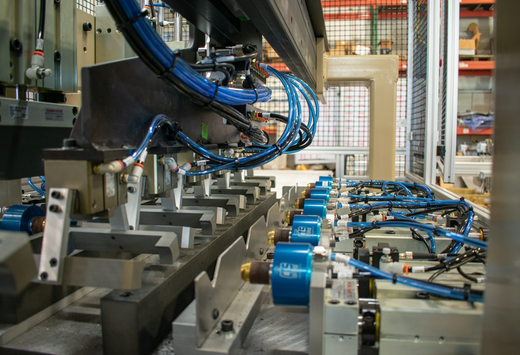 Close-up of automated industrial machinery with blue pneumatic cylinders and blue hoses connected. The focus is on the precision and automation involved in the industrial operation