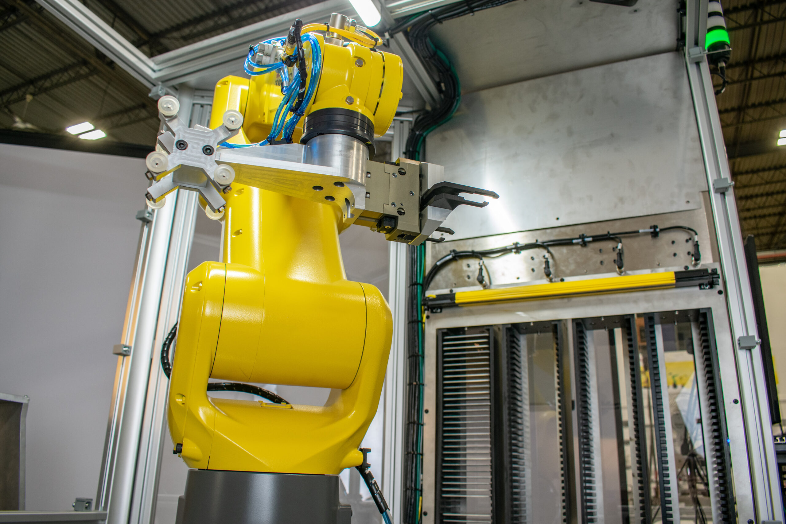 Yellow industrial robotic arm stands prominently inside a factory and features various attachments, including suction cups and pincer grips.