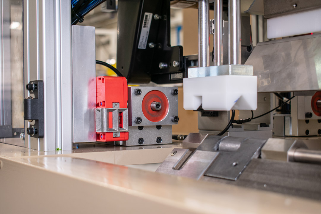 The machine features a series of metal and aluminum components, including sensors (some in bright red housings) and actuators.