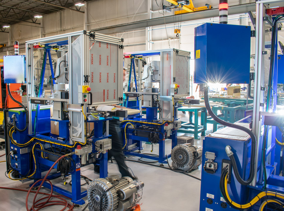 Robotic machinery with blue frames and silver enclosures are visible. Parts are moved along the line as each machine works on the specific part.