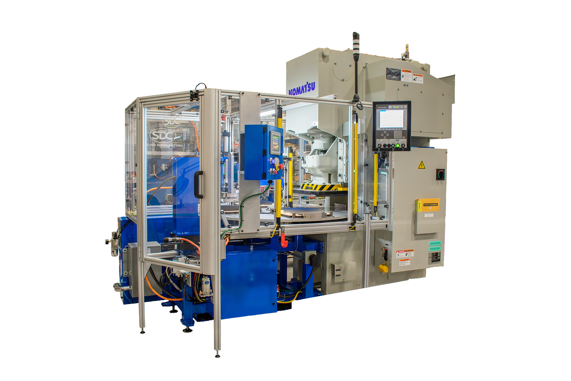 A large, automated Komatsu industrial machine with safety enclosure. The machine features a gray body, blue base, a protective cage made of translucent panels and metal framing, and an operator control panel with a digital screen.