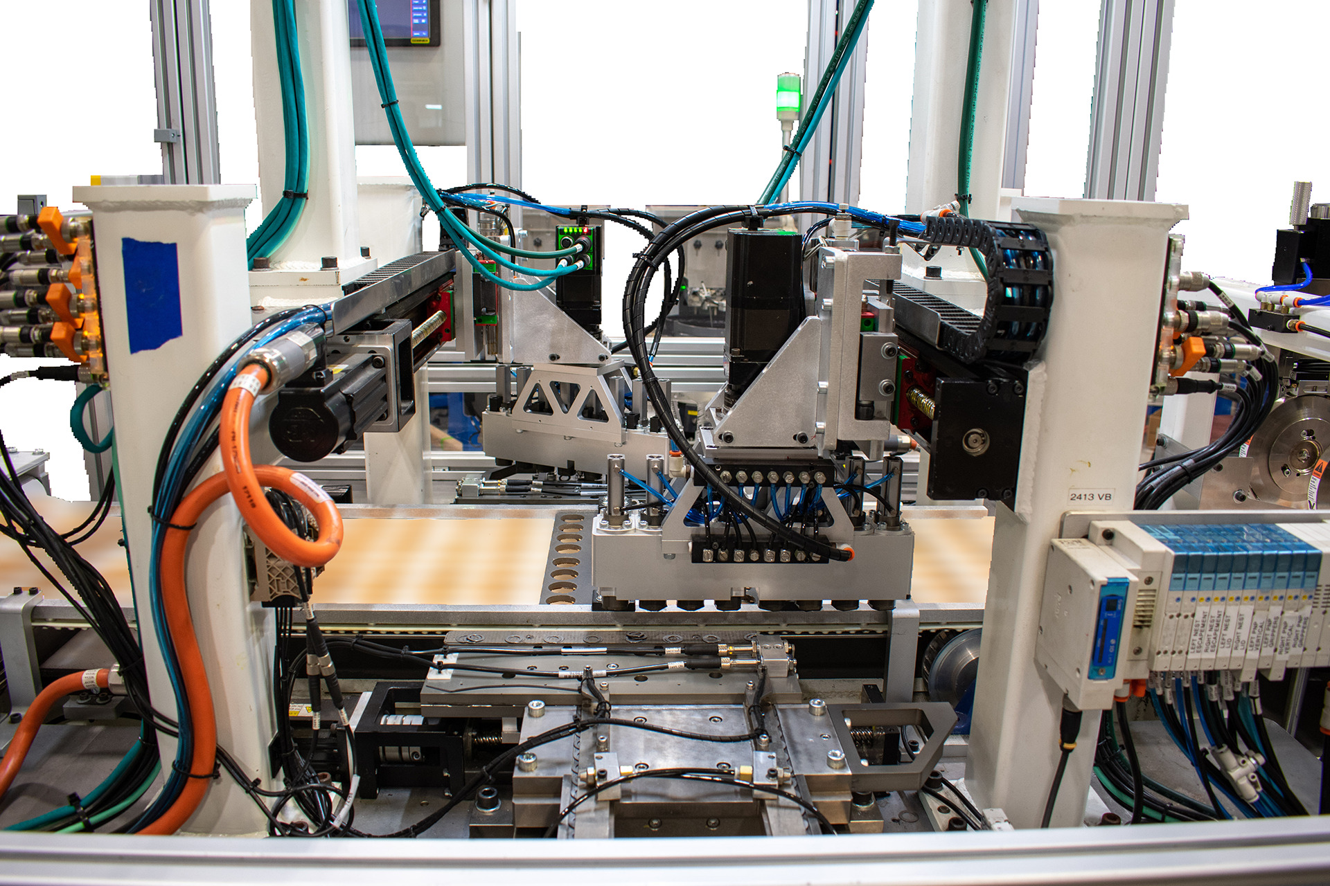 Close-up view of complex automated industrial machinery. Two robotic arms with specialized gripping mechanisms are positioned above a conveyor belt section filled with light colored rectangular material.