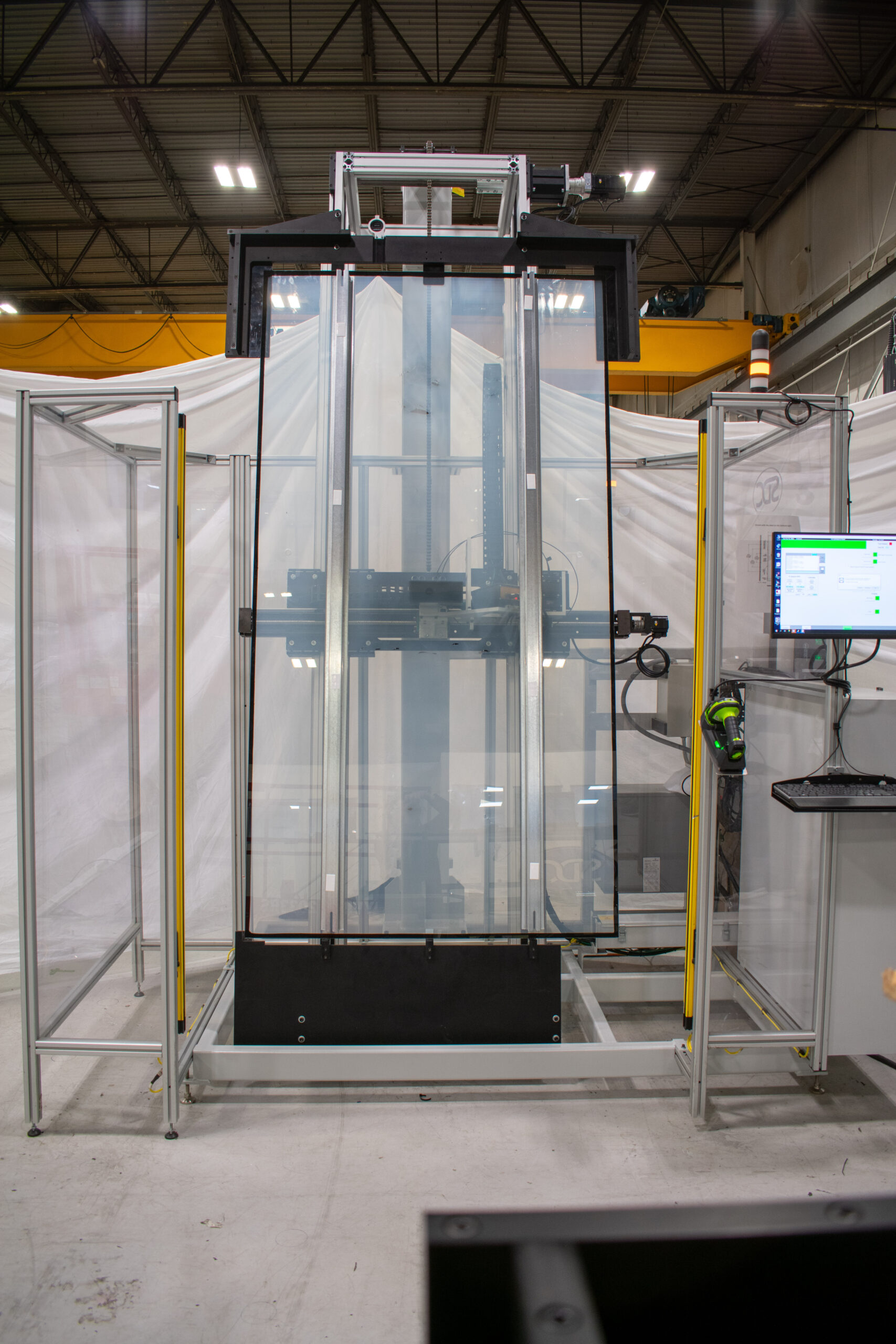 Clear glass pane is held vertically within a metal testing apparatus. The apparatus includes a black frame and mechanisms for moving and analyzing the glass.