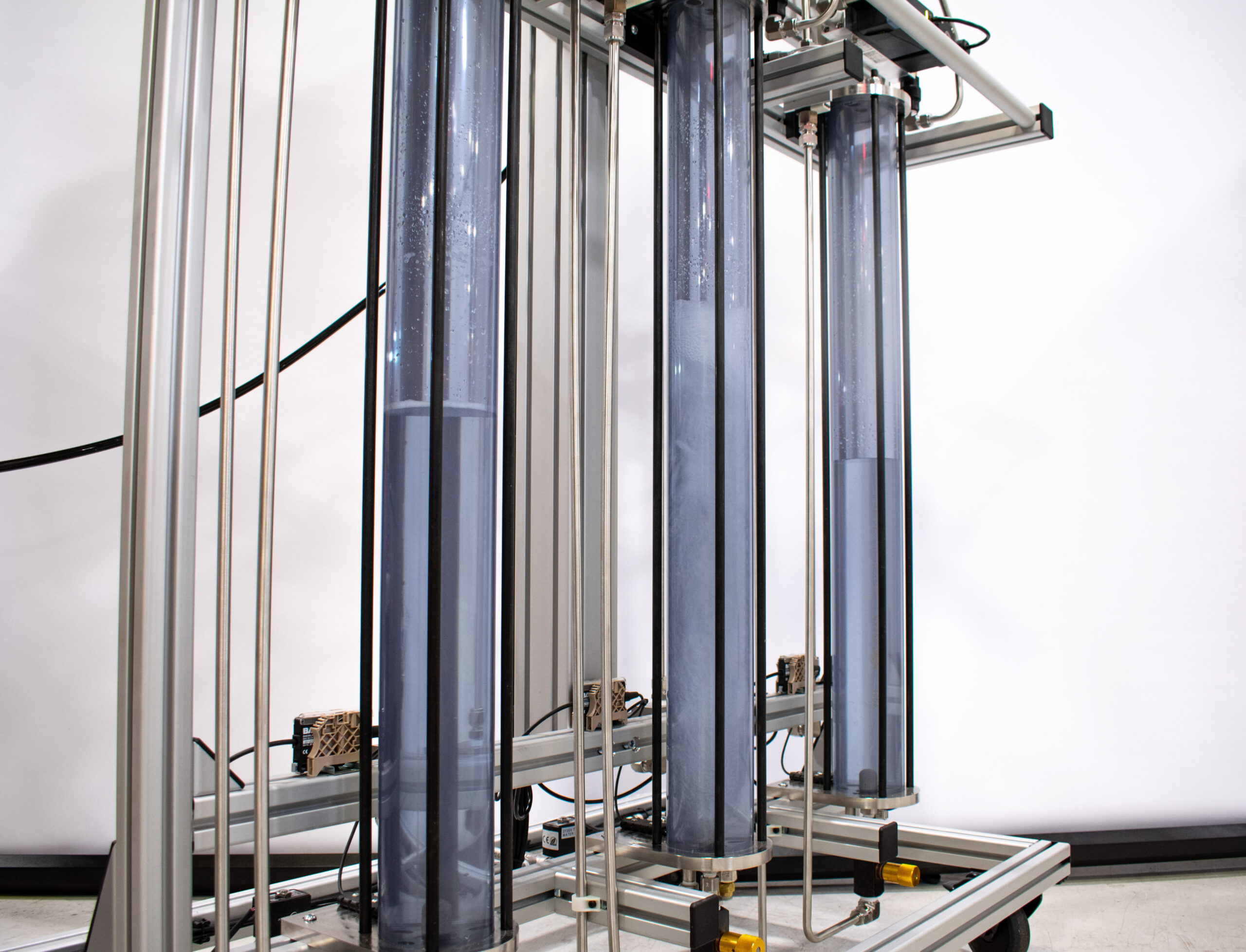 Fluid dynamics demonstration with three clear tubes and bubbling water, in a structural frame.