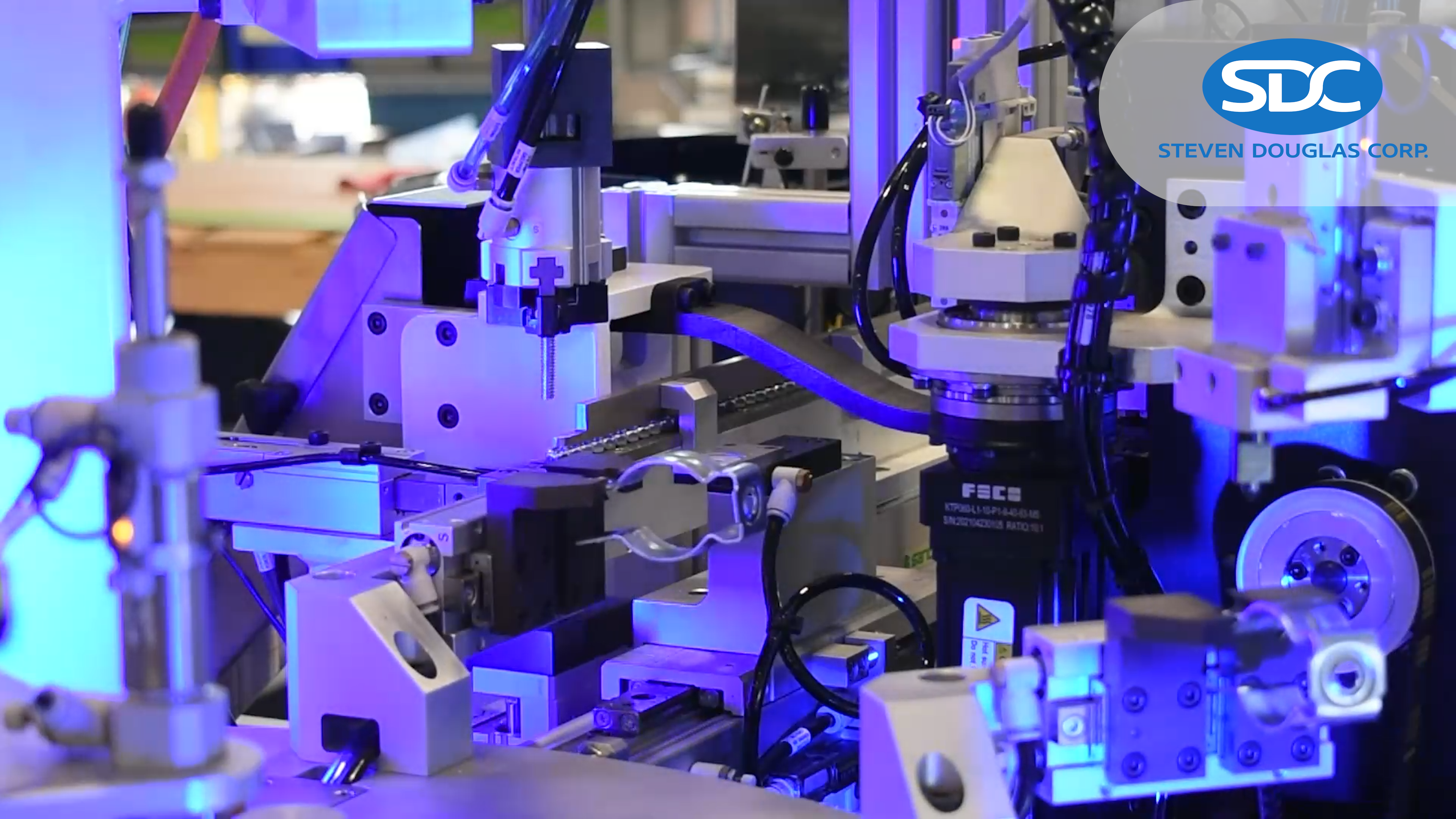 Close up of a complex automated industrial machine assembly process that is highlighted by blue LED lighting, showcasing various mechanical components with SDC logo.