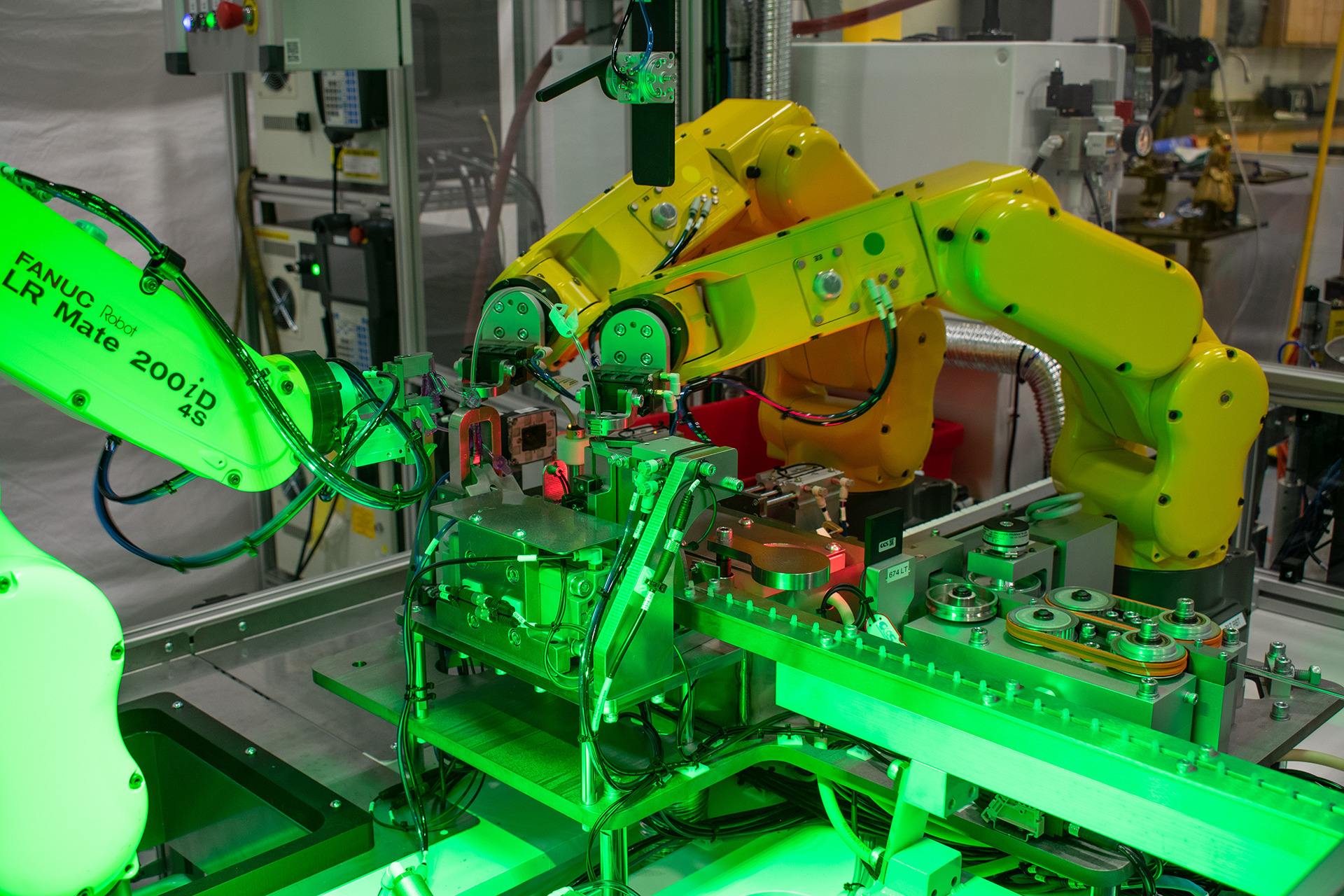 Bright green light is highlighting the machinery and the meticulous work being performed. Various belts, cogs, and control panels are visible, indicating an automated manufacturing process.