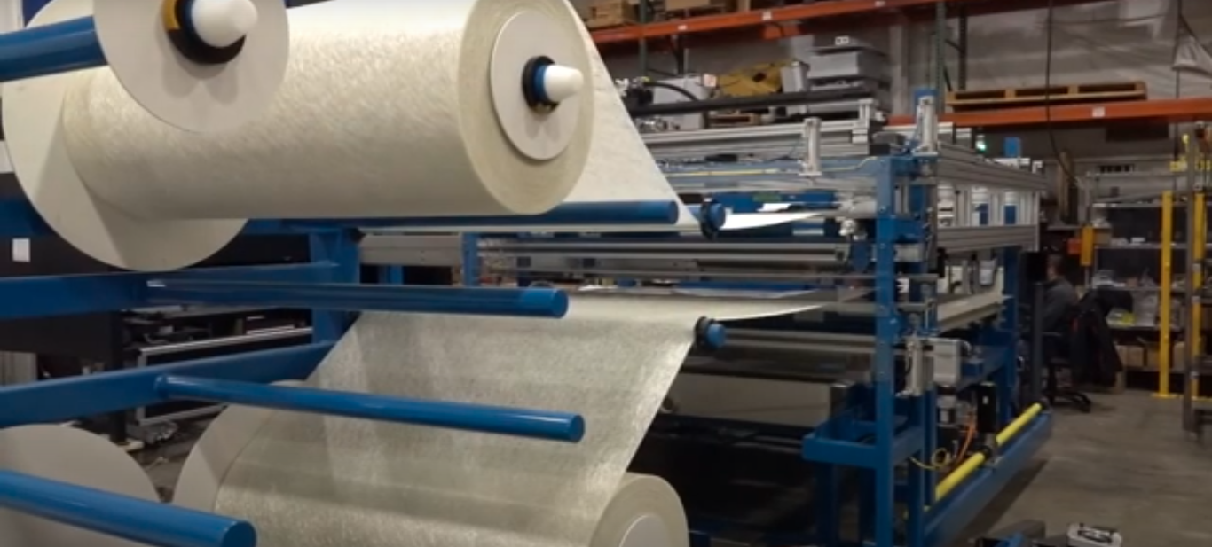 Close-up of industrial machine processing large rolls of fiberglass material in a factory setting.