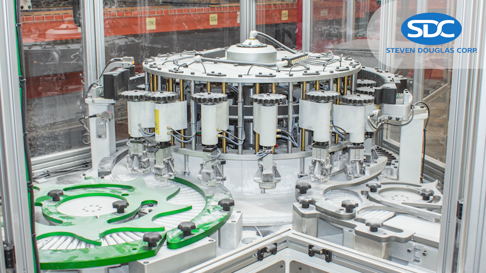 Machine of a central green, star-shaped wheel rotates, moving white filter-like materials into position for processing by a series of robotic arms with cylindrical white components.