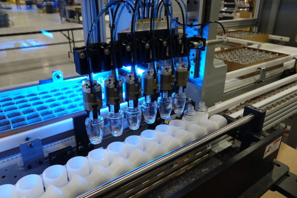 Automated bottling line: Robotic arms fill clear containers moving along a conveyor belt under bright blue lights.