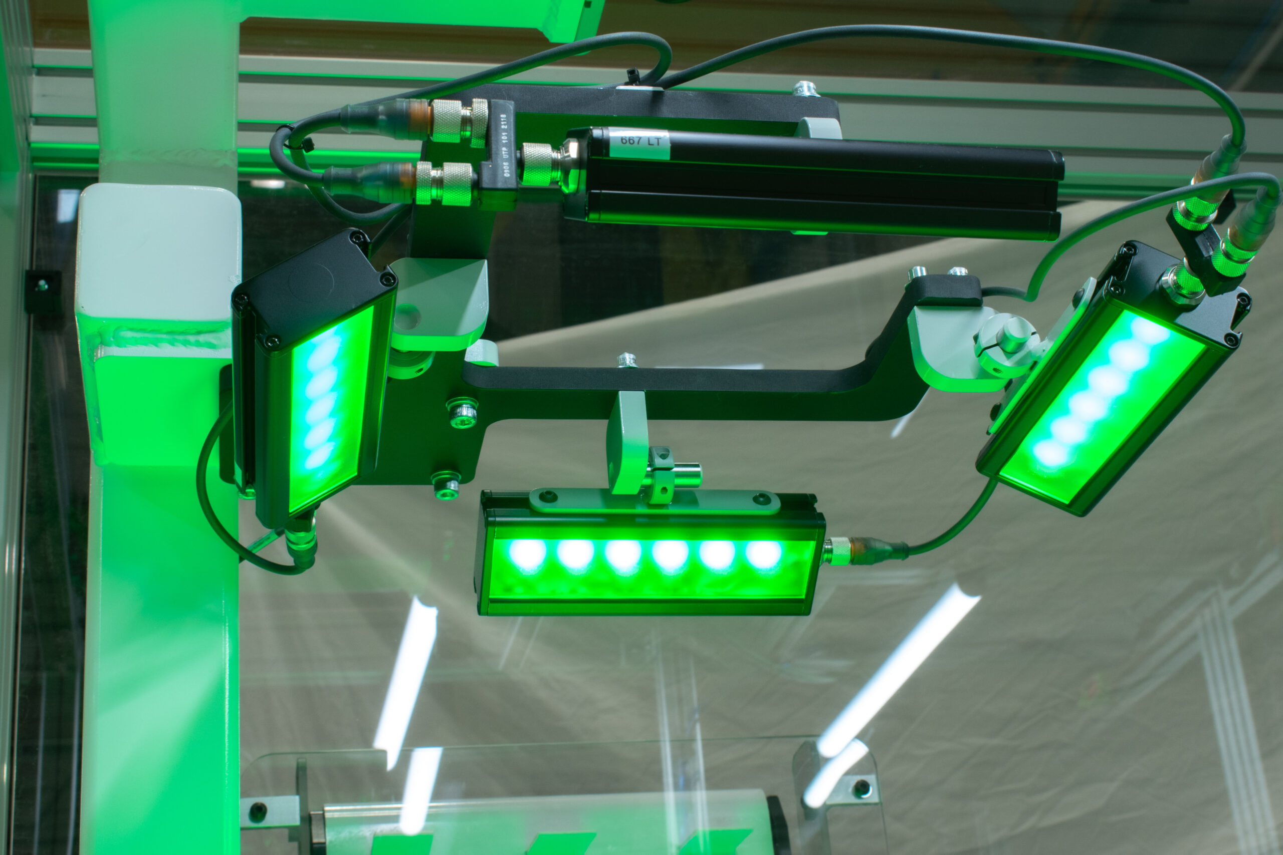 Industrial lighting array features black, rectangular housings holding green LED lights. They are mounted on a system with various adjustment points.