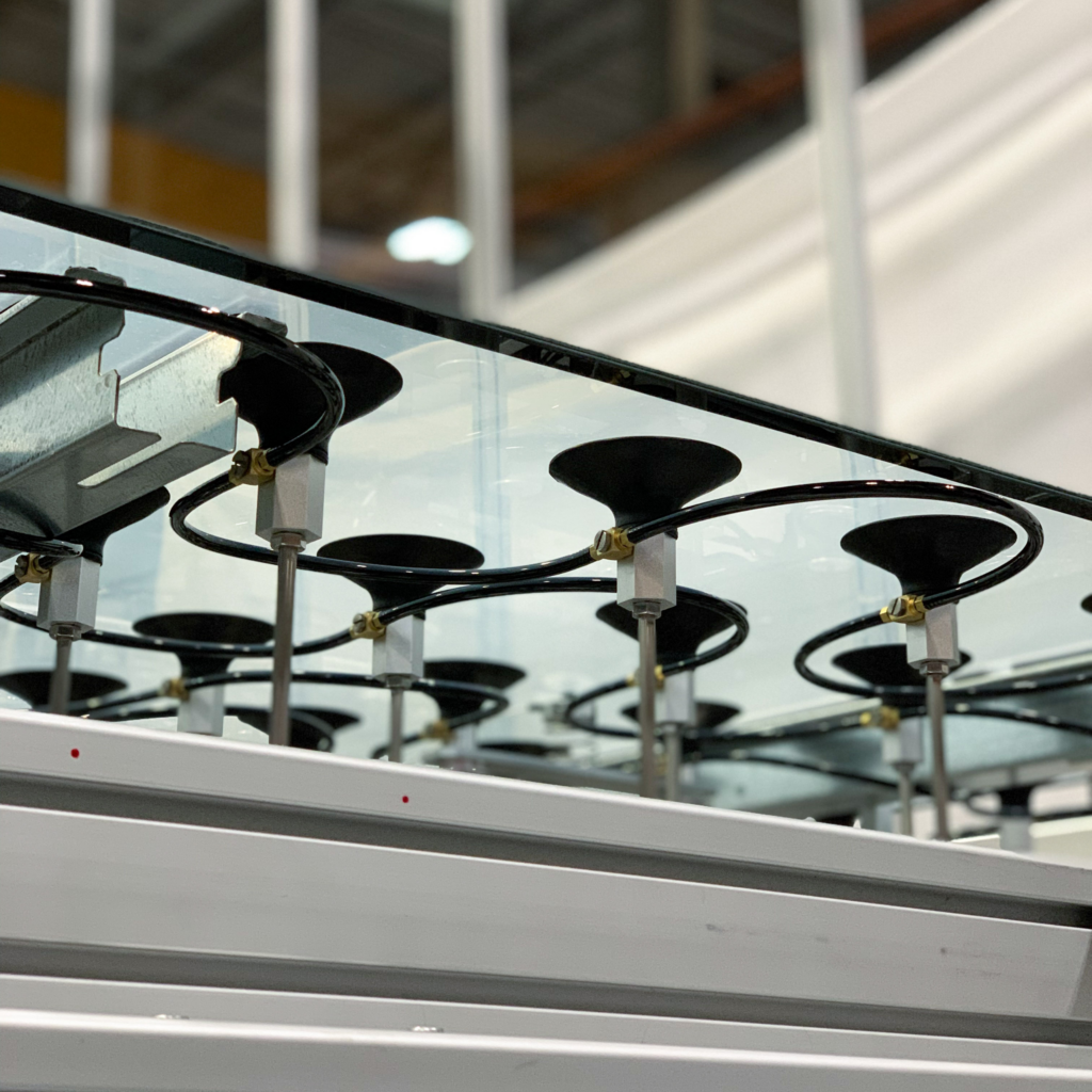 Series of black mounts are attached to a sheet of glass, held in place by thin metal rods and supported by a white, sturdy frame. The mounts are connected via small black tubing to a larger apparatus.