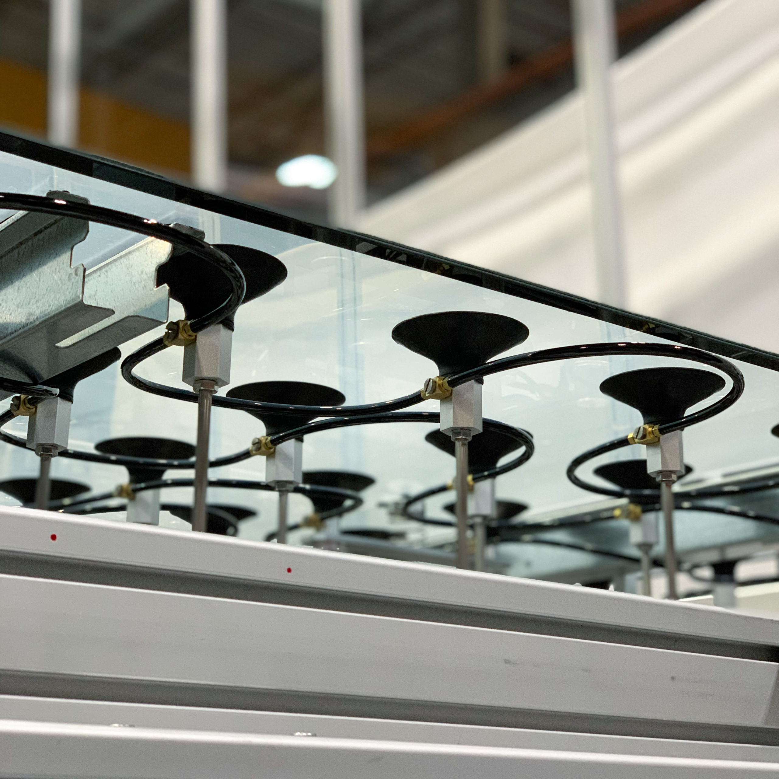Series of black mounts are attached to a sheet of glass, held in place by thin metal rods and supported by a white, sturdy frame. The mounts are connected via small black tubing to a larger apparatus.