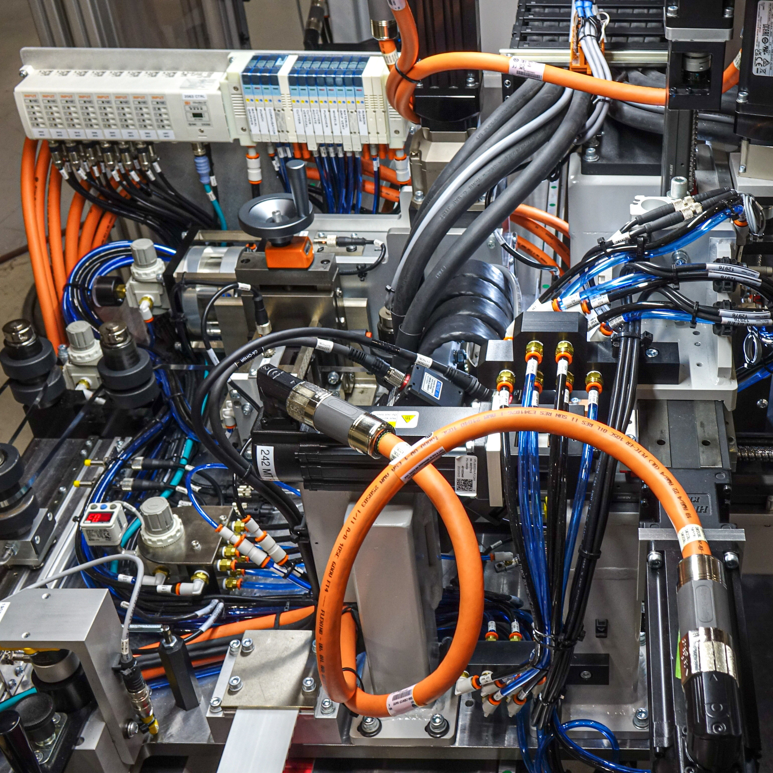 Close-up of complex automation equipment used in the aerospace industry. The image highlights the intricate network of wires, tubes, and mechanical components.