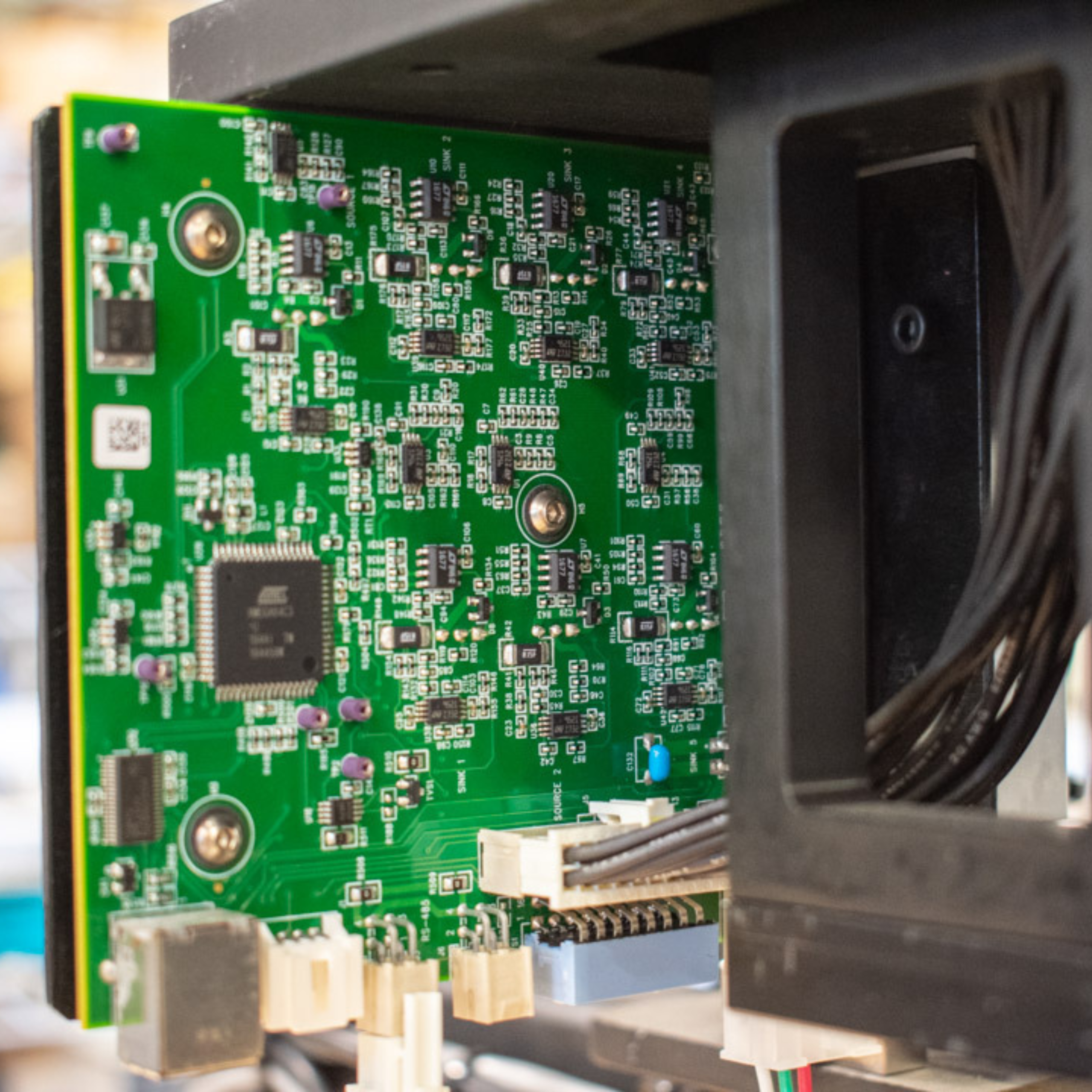 Green circuit board with various electronic components, connectors, and circuits. Board is inserted into a black chassis, with a bundle of connected cables visible.