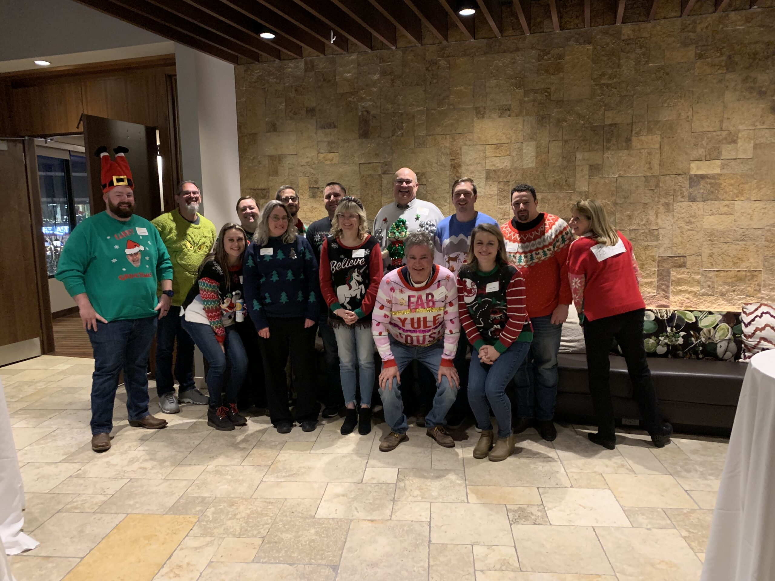 Group in ugly Christmas sweaters posing in front of a stone wall. Holiday party.