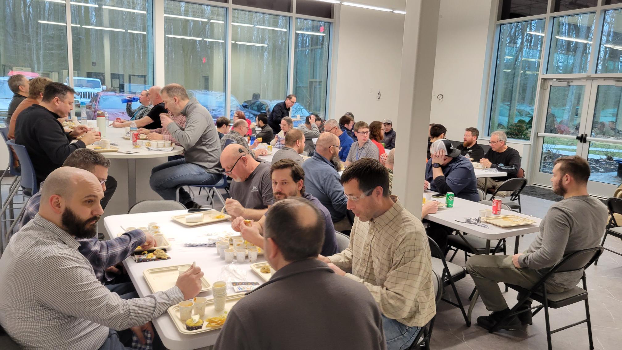 Group of people eating meal together at tables in a brightly lit room with large windows.