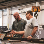 Two SDC employees talking about a project by a Waterjet machine