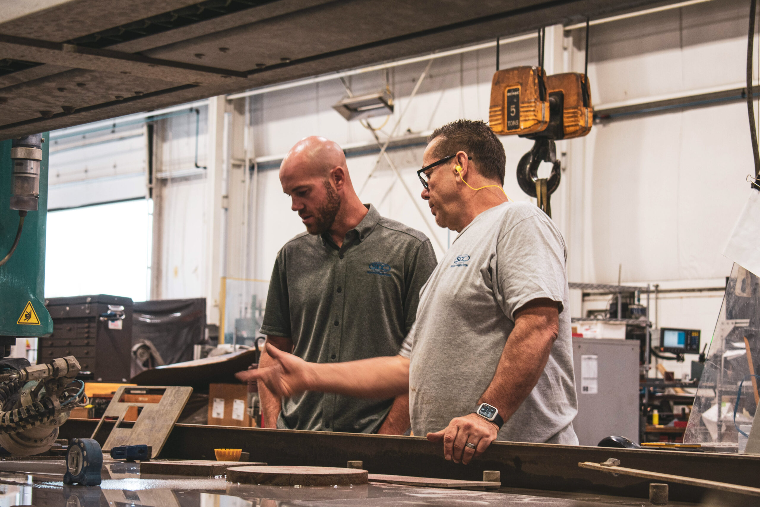 Two SDC employees talking about a project by a Waterjet machine