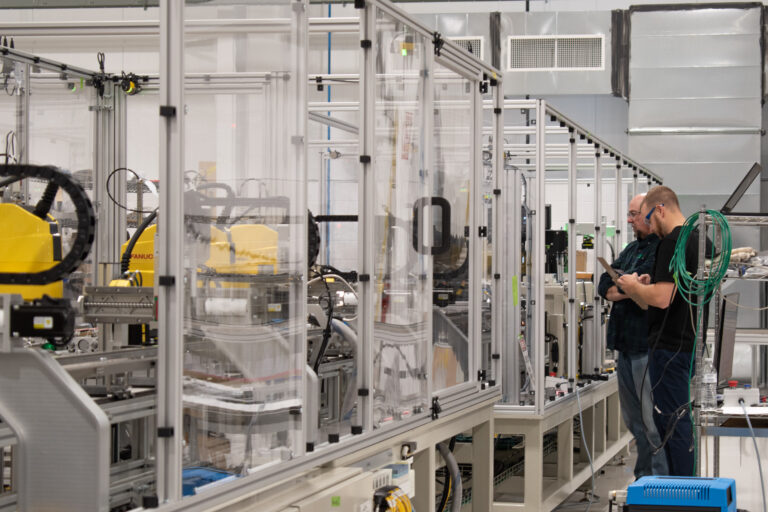 Two technicians inspect robotic machinery in a clean, modern lab setting.