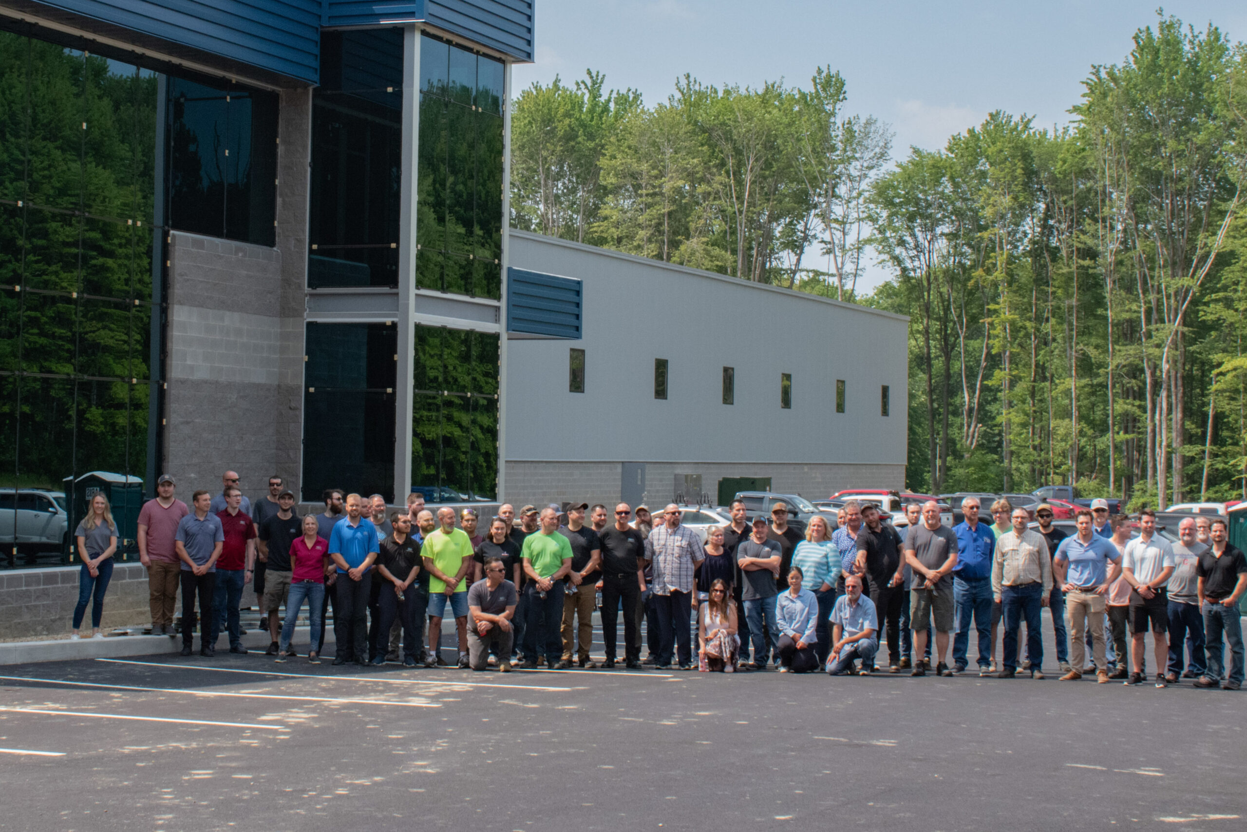 Group of SDC employees pose for a photo in front of their modern office building. The building features dark blue and gray facade and reflective glass windows.