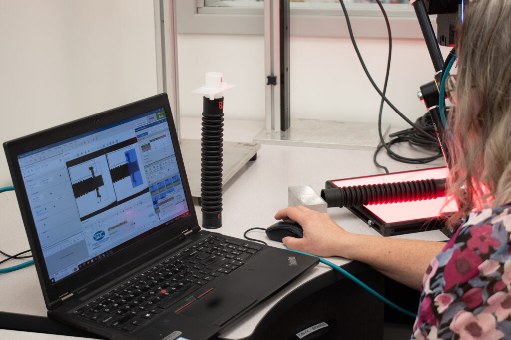 Industrial inspection setup: woman using laptop to analyze a corrugated tube under red light.