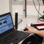 Industrial inspection setup: woman using laptop to analyze a corrugated tube under red light.