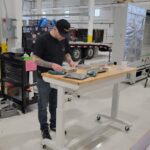 Technician with baseball hat looking down and measuring a component.