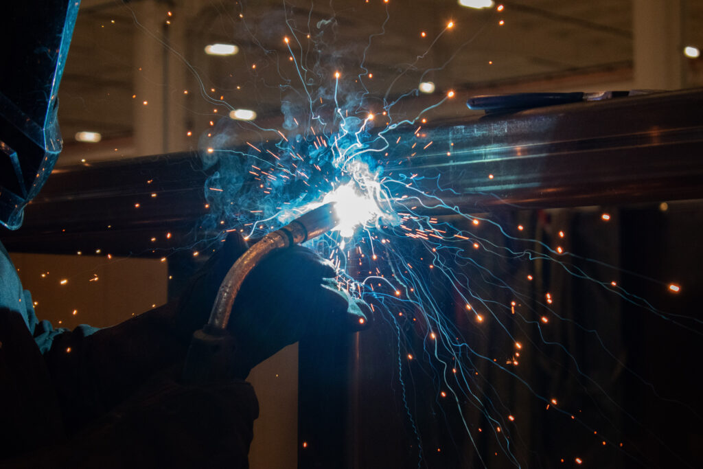 Close up image of a welder actively welding a part with sparks flying. 