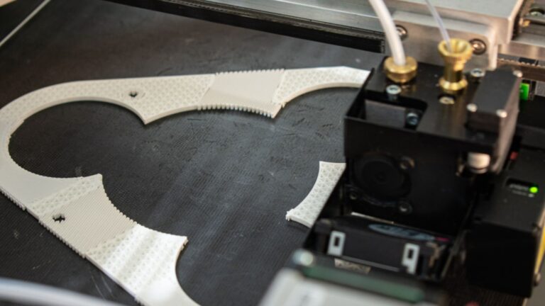 3D printer in motion making a white plastic part.
